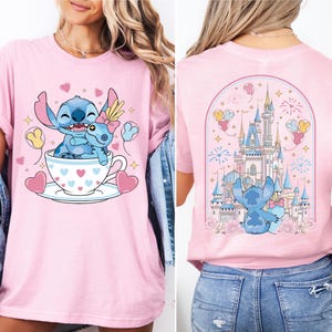 A woman wearing a pink t-shirt with a cartoon image of Stitch and her friends in a cup, along with a castle and fireworks in the background.