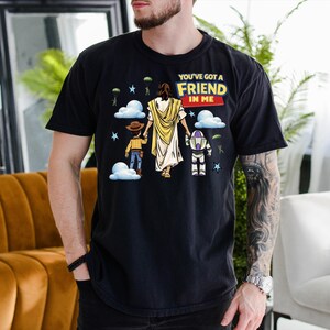 A man wearing a black t-shirt with a graphic design depicting a cartoon character and the text "You've got a friend in me"
