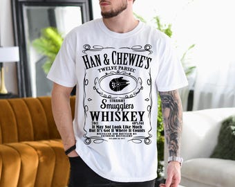 May include: White t-shirt with a black graphic of a whiskey label that says "Han & Chewie's Twelve Parsec Smugglers Whiskey 70cl 40% Vol It May Not Look Like Much But It's Got It Where It Counts Distilled and Bottled by Tatooine Distillery Est. ABY 1977"