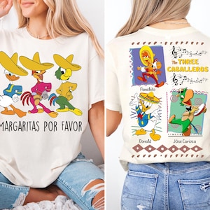 Puede incluir: Una camiseta blanca con un gráfico de Donald Duck, José Carioca y Panchito Pistoles de la película de Disney Los Tres Caballeros. El texto "Margaritas Por Favor" está impreso debajo del gráfico. La parte posterior de la camiseta presenta un gráfico de los tres personajes en cuadrados individuales con sus nombres debajo de cada uno. El texto "Los Tres Caballeros" está impreso encima de los cuadrados.