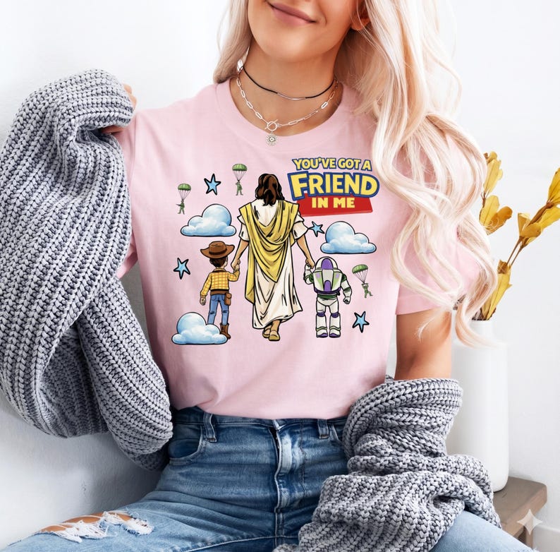 A woman wearing a pink t-shirt with a cartoon illustration of Jesus Christ and two children, along with the text "You've Got a Friend in Me".