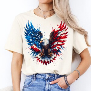 A woman wearing a white t-shirt with an American eagle design and jeans stands against a white background.