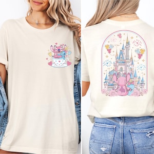 A woman wearing a white t-shirt with a graphic design of a castle and two pink characters on the back.