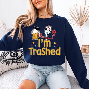 A woman wearing a navy blue sweatshirt with a graphic design of a character from the Toy Story franchise and the text "I'm Trashed" printed on it.