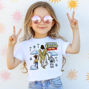 A young girl wearing a white t-shirt with a graphic design and making a peace sign with her hands.