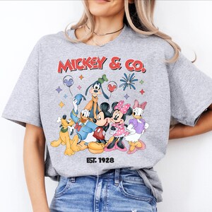A woman wearing a gray t-shirt with a graphic of Disney characters and text.