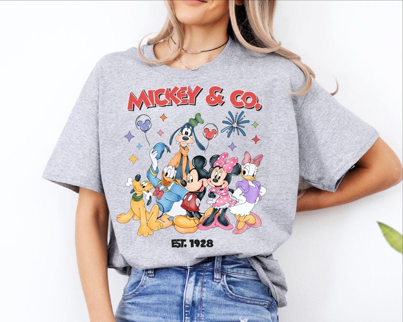 A woman wearing a gray t-shirt with a graphic of Disney characters and text.