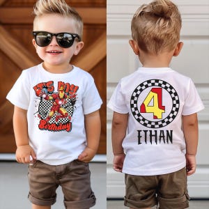 A young boy wearing a white t-shirt with a graphic design and sunglasses, standing in front of a wooden door.