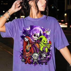May include: A purple short-sleeve t-shirt featuring a graphic print of characters from The Nightmare Before Christmas, including Jack Skellington, Sally, Oogie Boogie, and others, set against a purple moonlit background with bats and a spiderweb.