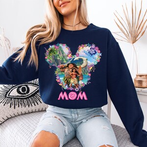 a woman sitting on a bed wearing a mickey mouse sweatshirt
