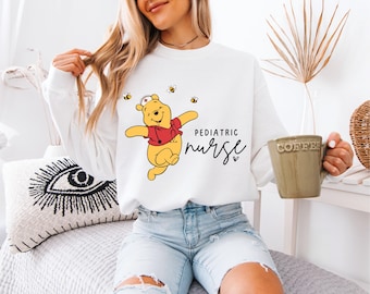 May include: White sweatshirt with a cartoon Winnie the Pooh dressed as a nurse and the text "Pediatric nurse" with a heart.