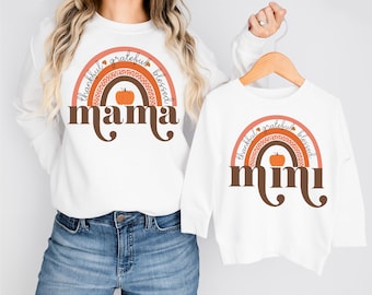 May include: White sweatshirts with matching rainbow designs. The adult sweatshirt says "mama" with a pumpkin in the centre of the rainbow. The child's sweatshirt says "mimi" with a pumpkin in the centre of the rainbow. The rainbow design includes the words "thankful, grateful, blessed."