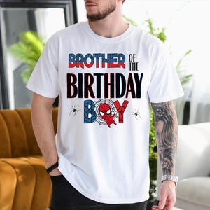 A man wearing a white t-shirt with a graphic design that says "BROTHER OF THE BIRTHDAY BOY" and Spider-Man imagery.