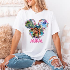 a woman sitting on a bed wearing a mickey mouse shirt