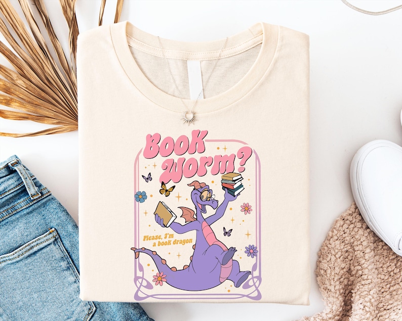 a white t-shirt with a cartoon dragon holding a book, surrounded by butterflies and flowers, along with the text "Book Worm?"