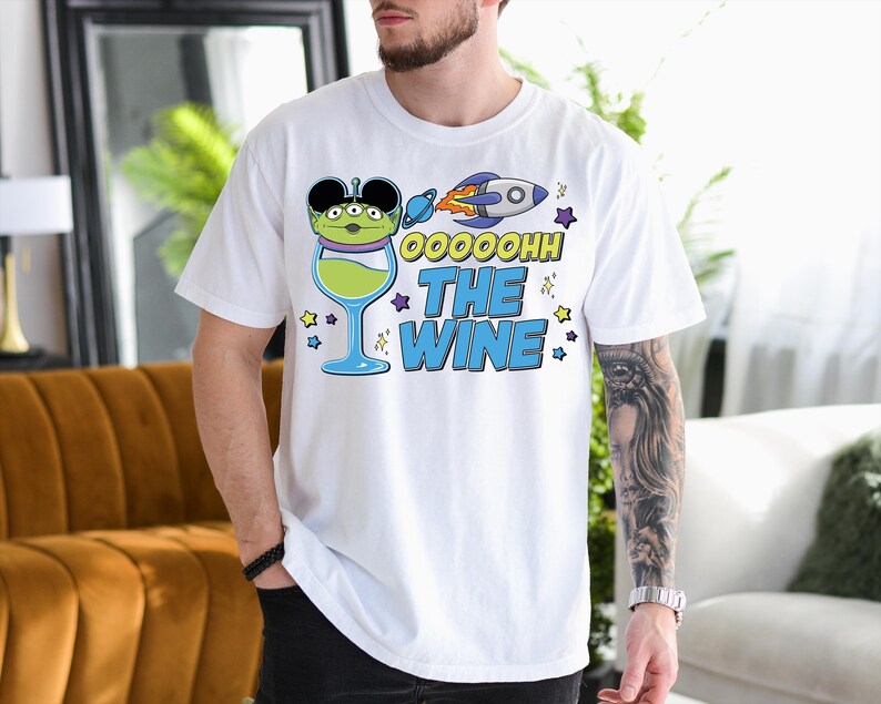A man wearing a white t-shirt with a graphic design featuring a green alien character and a rocket ship, along with the text "OOOHOH THE WINE".