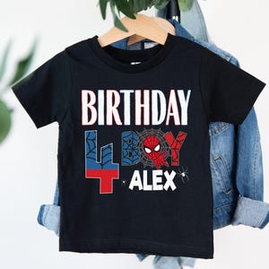 A black t-shirt with a Spider-Man design and text printed on it, hanging on a clothing hanger.
