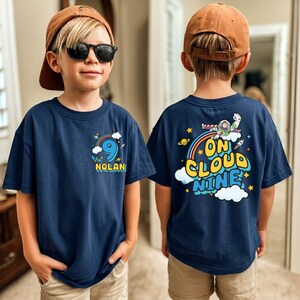 A young boy wearing a navy blue t-shirt with a graphic design and text on the back, standing in front of a mirror.