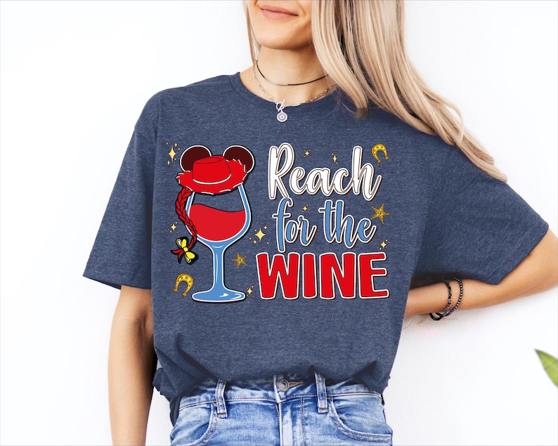 A woman wearing a blue t-shirt with a graphic design that says "Reach for the WINE" and features a wine glass and a character resembling Mickey Mouse.