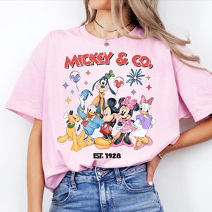 A woman wearing a pink t-shirt with a graphic of Disney characters Mickey Mouse and Co.