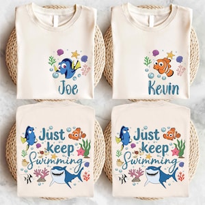 May include: Four cream-colored t-shirts with Finding Nemo designs. Two shirts feature the names "Joe" and "Kevin" with cartoon fish. The other two shirts say "Just keep Swimming" with Nemo, Dory, and a shark.