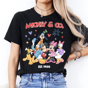 A woman wearing a black t-shirt with a graphic of Disney characters and the text "MICKEY & CO." printed on it.