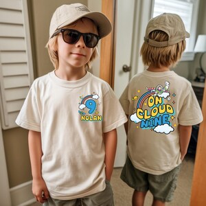A young boy wearing a white t-shirt with a number 9 and a cloud graphic, standing in a room with a door and a window in the background.