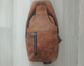 Puede incluir: Un bolso de bandolera de cuero marrón con una cremallera negra y un tirador de cremallera plateado.