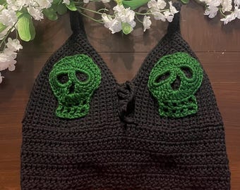 May include: Black crochet top with green skull details. The top has a lace-up front and a scalloped hem.