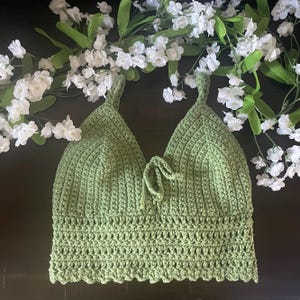May include: A green crocheted halter top with a tie at the front. The top has a scalloped hem and is made with a soft, textured yarn.