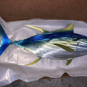 May include: A metal sculpture of a tuna fish with blue, green, and yellow paint. The fish is depicted in a realistic style with detailed scales and fins.