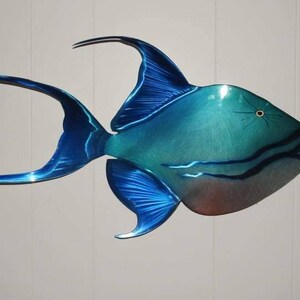 May include: A blue and green metal sculpture of a triggerfish. The fish has a long, thin tail and a large, round body. The sculpture is painted with a metallic finish and has a realistic appearance.