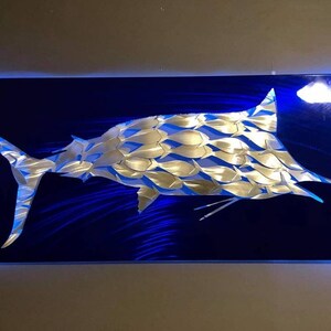 Puede incluir: Una escultura de marlin de metal plateado sobre un fondo azul. El marlin est&aacute; hecho de muchas peque&ntilde;as formas de peces.