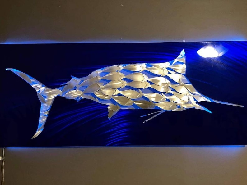 Puede incluir: Una escultura de marlin de metal plateado sobre un fondo azul. El marlin est&aacute; hecho de muchas peque&ntilde;as formas de peces.