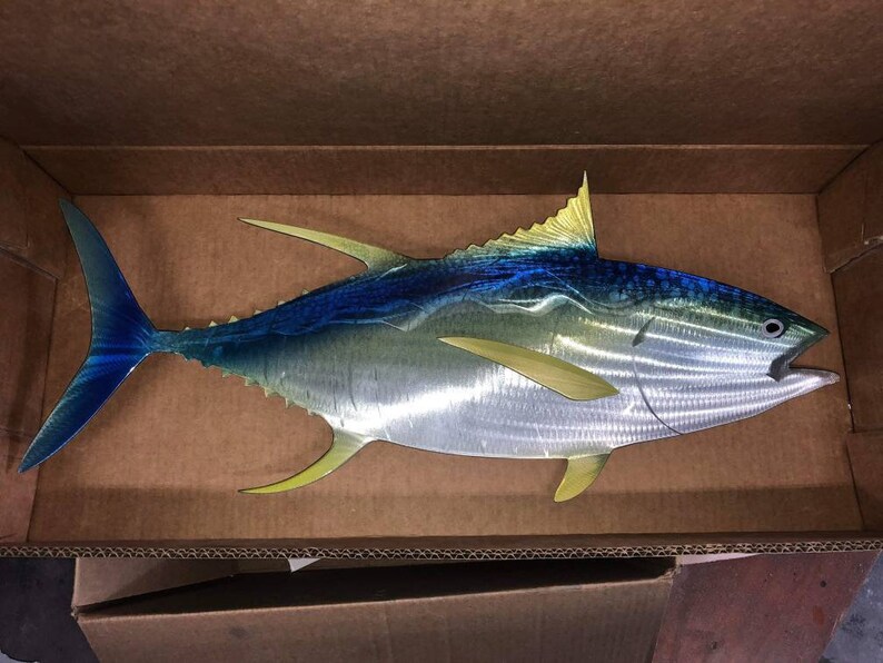 May include: A metal sculpture of a yellowfin tuna fish with blue and yellow accents. The fish is in a cardboard box.