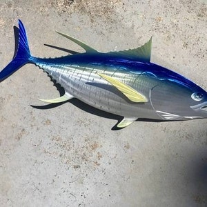 May include: A metal sculpture of a blue and silver tuna fish with yellow fins. The fish is mounted on a gray background.