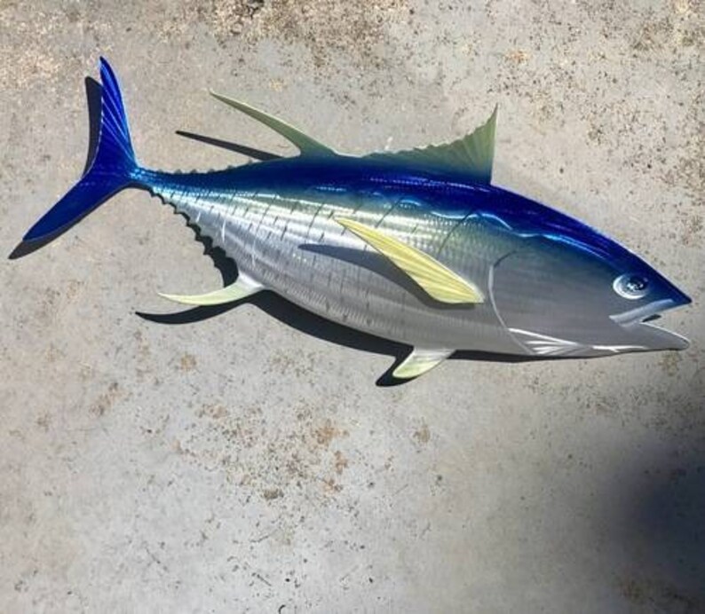 May include: A metal sculpture of a blue and silver tuna fish with yellow fins. The fish is mounted on a gray background.