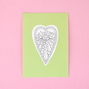 Puede incluir: Una tarjeta verde con una ilustración en blanco y negro de un corazón con llamas y un ojo en su interior. El corazón está rodeado por una cadena.