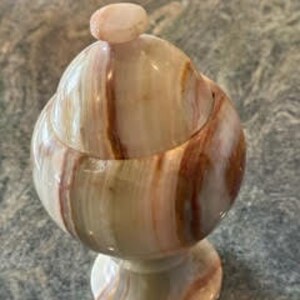 May include: A decorative, round, green, brown, and white marble jar with a lid. The jar has a pedestal base.