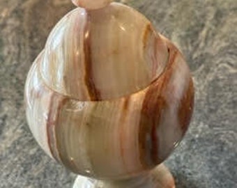 May include: A decorative, round, green, brown, and white marble jar with a lid. The jar has a pedestal base.