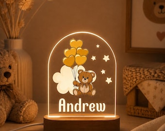 May include: An arched acrylic night light with a wooden base featuring a printed illustration of a brown teddy bear holding a cluster of yellow heart-shaped balloons near a white cloud and stars, with the name Andrew printed in white lettering.