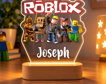 May include: A custom LED night light featuring the Roblox logo and five colorful character figures. The acrylic panel displays the name Joseph in white script font, mounted on a light-colored wooden base that illuminates the design from below.