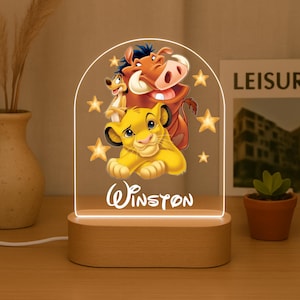 Puede incluir: Luz de noche decorativa con base de madera y panel acrílico transparente. El panel presenta personajes de El Rey León, incluyendo a Simba, Timón y Pumba, con el nombre "Winston". El diseño incluye estrellas.