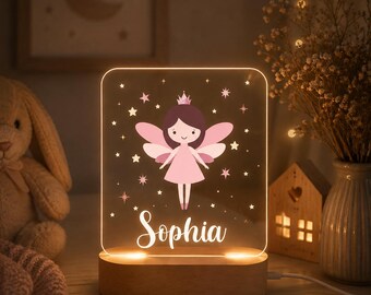 May include: A rectangular acrylic night light with a wooden base, featuring a printed illustration of a fairy with brown hair and a pink dress, surrounded by small stars. The name Sophia is printed in white script lettering at the bottom.