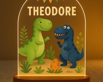 Könnte beinhalten: Dekoratives Nachtlicht mit zwei Zeichentrick-Dinosauriern, einem grünen und einem blauen, mit dem Namen "THEODORE" darüber. Das Licht hat einen Holzsockel und eine transparente Acrylplatte mit farbenfrohem Design.