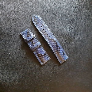 May include: Two-piece watch strap in a blue snakeskin pattern. The strap is made of a textured material with a dark blue and black color scheme. The strap has several holes for adjustment and a buckle.