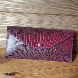 May include: A purple snakeskin wallet with a flap closure and a single button.