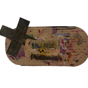 May include: A brown cardboard rectangle with a rusty metal cross, a yellow tag with the text "BE LARGE" and paint splatters in various colors.