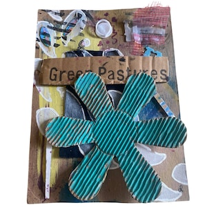 May include: A mixed media collage featuring a large teal blue cardboard flower with a corrugated texture. The flower is layered on top of a brown cardboard background with various textures and colors, including yellow, white, and black. The text "Green Pastures" is visible on the cardboard background.