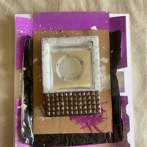 May include: A mixed media collage featuring a white square with a round mirror inside, a brown studded surface, and a black and white sign with the text "faisons quelque chose de different".